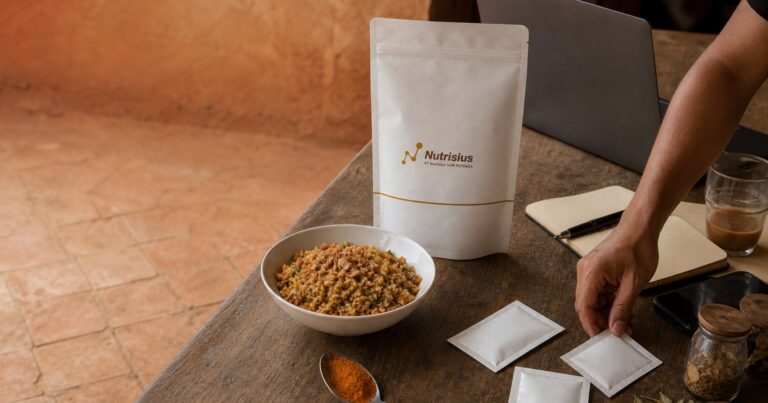 Pouch bumbu nasi goreng, nasi goreng matang, dan sachet sampel di meja kerja.